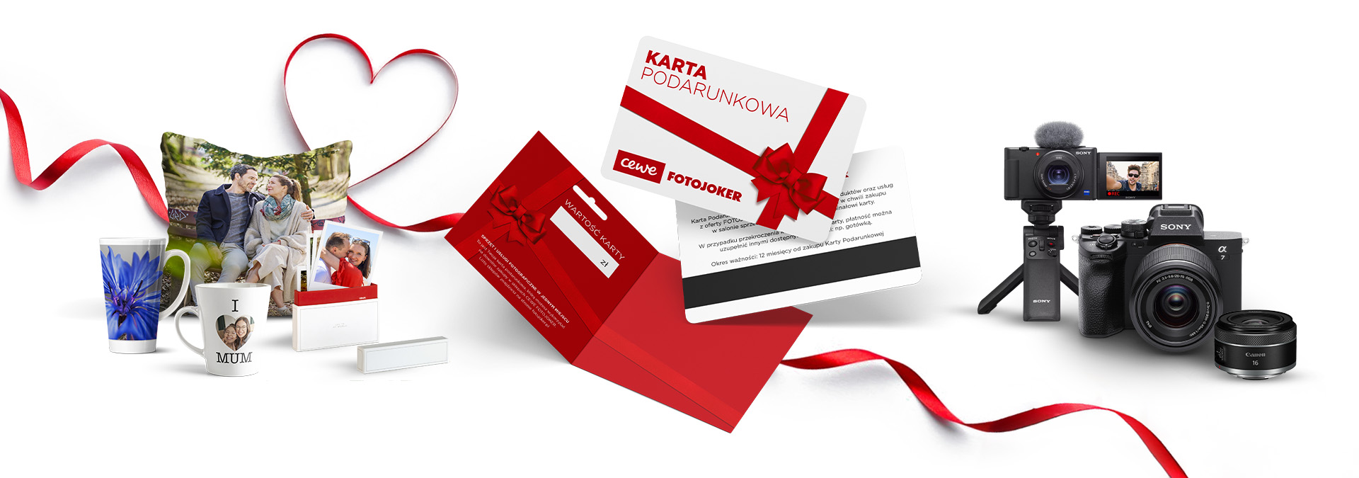 Poduszka z nadrukiem pary, kubki z personalizowanymi zdjęciami, album fotograficzny, karty podarunkowe CEWE z czerwoną kokardą, aparat fotograficzny z akcesoriami oraz czerwona wstążka w formie serca